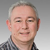 Der Mann hat ein freundliches Lächeln und zeigt eine entspannte Haltung, während er in die Kamera schaut.