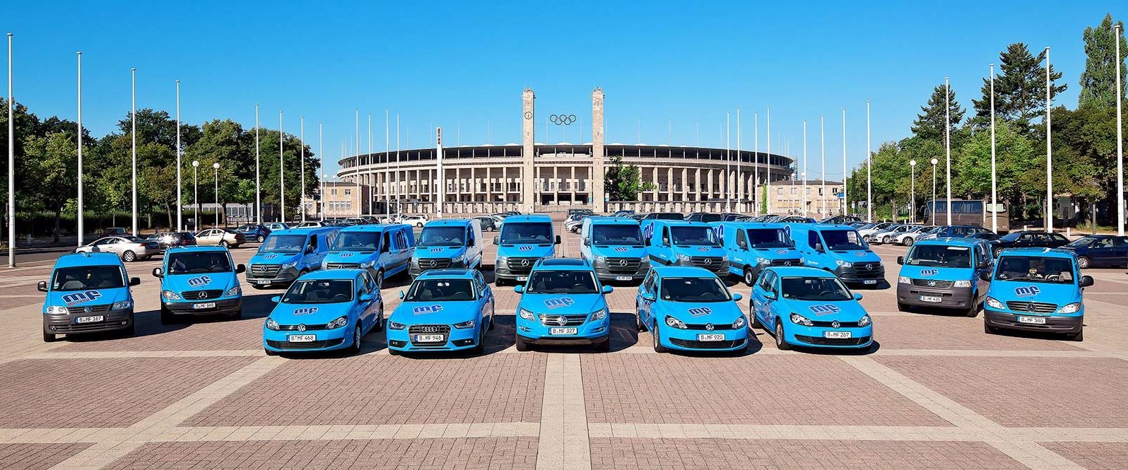 Blaue Fahrzeuge vor dem Olympiastadion in Berlin Verschiedene blaue Autos und Vans sind auf einem Platz angeordnet, mit einem großen Stadion im Hintergrund.