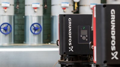 Im Vordergrund sind mehrere schwarze Pumpen mit orangefarbenen Dichtungen zu sehen, im Hintergrund stehen silberne Rohre.