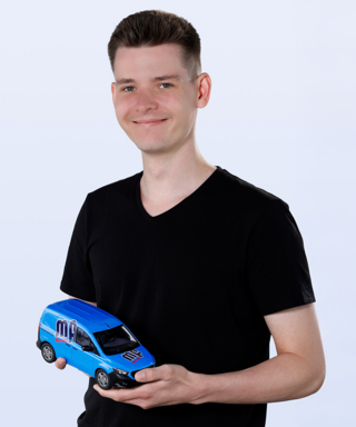 Junger Mann hält ein blaues Modellauto in der Hand Ein junger Mann mit kurzem Haar lächelt, während er ein blaues Modellauto in den Händen hält.