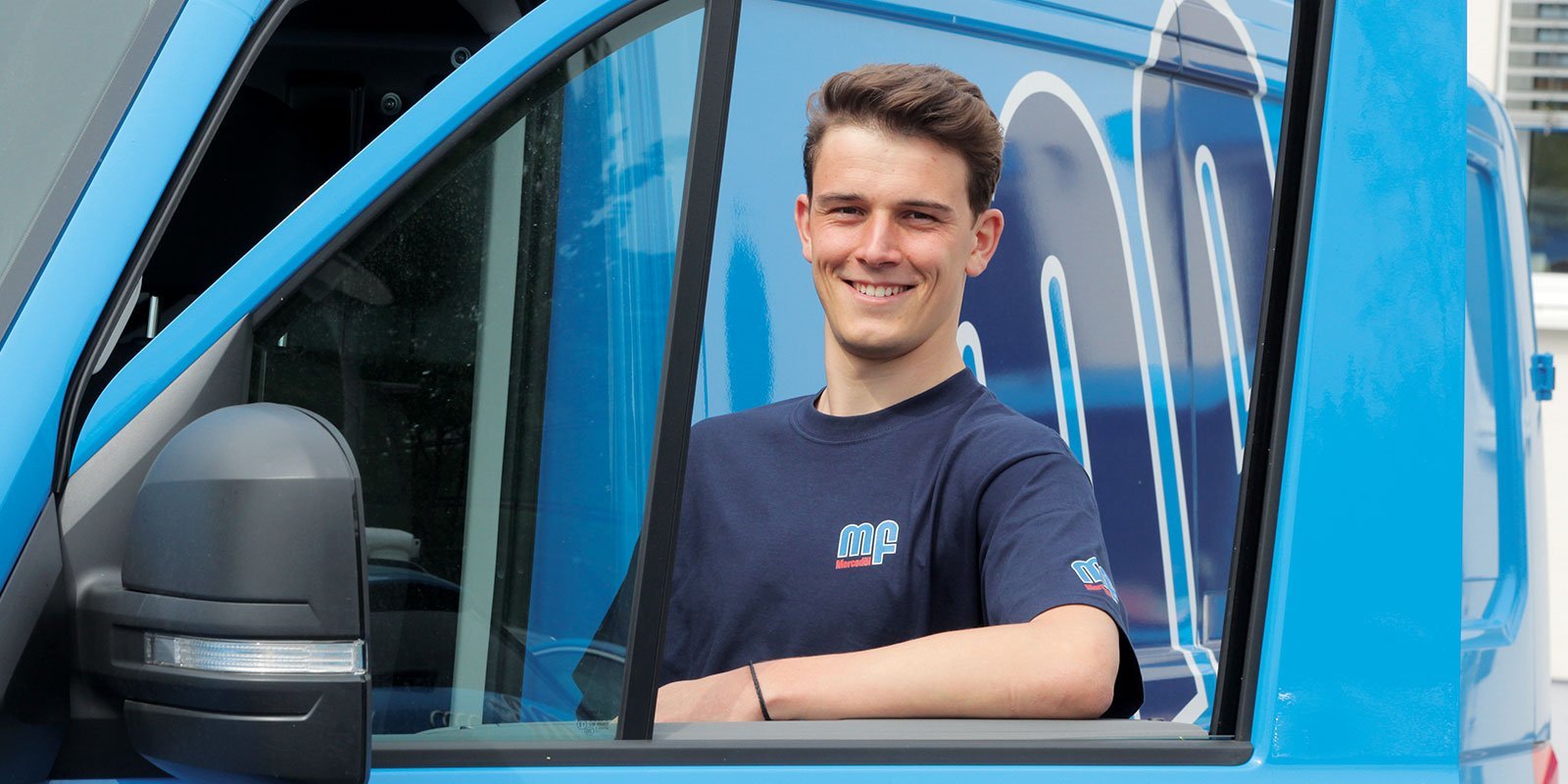 Der Fahrer eines blauen Vans zeigt ein freundliches Lächeln, während er mit einem Arm auf das Fenster gestützt ist.
