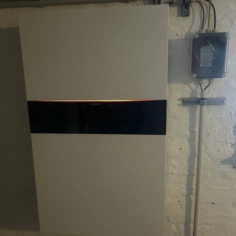 Ein modernes, weißes Gerät an der Wand mit einem schwarzen Bedienfeld und einer leuchtenden Anzeige in einem Keller.