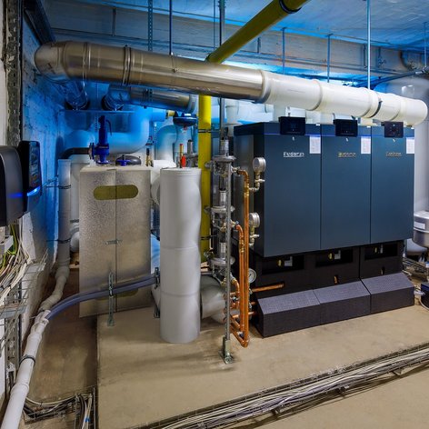 In einem gut beleuchteten Heizungsraum sind verschiedene Heizkessel und Rohre sichtbar, die für die Energieversorgung sorgen.