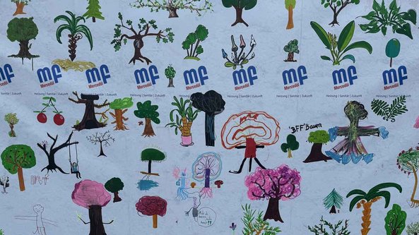Eine bunte Wandmalerei mit verschiedenen Bäumen, Pflanzen und kindlichen Zeichnungen, die eine lebendige Natur darstellt.