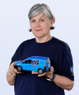 Frau hält ein Modell eines blauen Lieferwagens in der Hand Eine ältere Frau hält ein blaues Modellauto in den Händen und schaut direkt in die Kamera mit einem neutralen Gesichtsausdruck.
