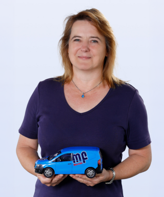 Frau hält ein blaues Modellauto in der Hand Die Frau trägt ein lila T-Shirt und zeigt stolz ein kleines, blaues Lieferfahrzeug mit dem Logo 'Mercedes'.