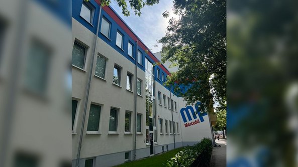 Ein modernes Gebäude mit blauer und roter Fassade, umgeben von Bäumen und einem gepflegten Gehweg.