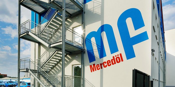 Eine moderne Gebäudeansicht mit einer großen, blauen Schrift, die 'mf' und 'Mercedöl' zeigt, umgeben von einer Stahltreppe.
