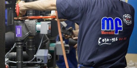 In einer technischen Umgebung repariert ein Handwerker mit einem Werkzeug eine Maschine, während andere Mitarbeiter helfen.