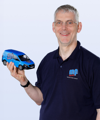 Mann mit Modellauto in blauer Arbeitskleidung lächelt Ein lächelnder Mann hält ein Modell eines blauen Lieferwagens in der Hand, während er in einem dunklen Poloshirt steht.