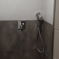 Ein moderner Duschbereich mit grauen Fliesen und einem eleganten Duschkopf an der Wand, der eine minimalistische Atmosphäre schafft.