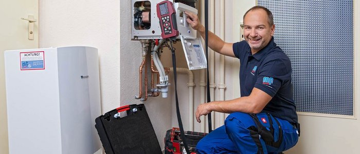 Handwerker überprüft Heizungsgeräte in einem Wohnraum Ein Handwerker überprüft eine Heizungsanlage, während er lächelnd auf dem Boden sitzt und Werkzeuge in einer Tasche sortiert.