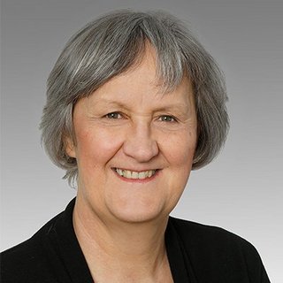 Professionelles Porträt einer lächelnden Frau mit grauen Haaren Die Frau mit kurzen grauen Haaren strahlt Selbstbewusstsein aus und posiert vor einem neutralen Hintergrund.