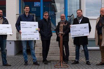 Die Gewinner des EVENTUS-PREIS 2021 posieren lächelnd vor einem Eingang, während sie ihre Auszeichnungen präsentieren.