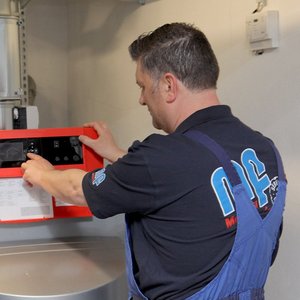 Zwei Männer stehen in einem technischen Raum und überprüfen gemeinsam ein rotes Bedienfeld an einer Maschine.