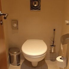 Der Innenraum eines kleinen Badezimmers, das eine saubere Toilette und einen glänzenden Mülleimer zeigt.