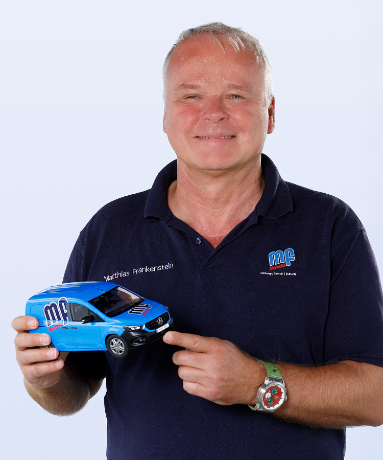 Ein Mann lächelt, während er ein blaues Modellauto in der Hand hält, das ein Firmenlogo trägt.
