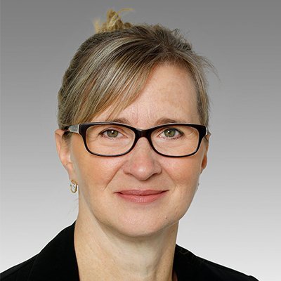 Eine Frau mit Brille lächelt freundlich in die Kamera, ihre Haare sind zu einem lockeren Dutt frisiert.