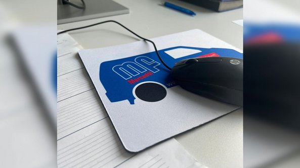  Eine schwarze Computermaus liegt auf einem Mauspads mit einem blauen Fahrzeugdesign und dem Schriftzug 'Mercedoel'. 