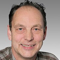 Ein lächelnder Mann mit kurzen, lockigen Haaren trägt ein kariertes Hemd und hat einen freundlichen Gesichtsausdruck.