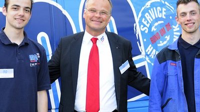 Drei Männer stehen lächelnd vor einem blauen Lieferwagen, der mit dem Logo und Slogan des Unternehmens versehen ist.