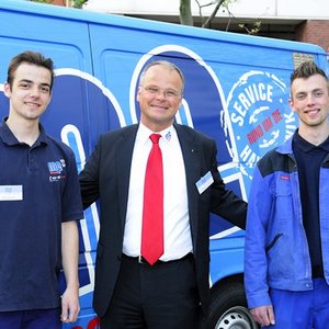 Drei Männer stehen lächelnd vor einem blauen Lieferwagen, der mit dem Logo und Slogan des Unternehmens versehen ist.
