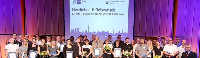 Feierliche Ehrung der besten Ausbildungsbetriebe in Berlin Eine Gruppe von Menschen steht auf einer Bühne, stolz mit Urkunden und Blumen, während sie für eine Auszeichnung posieren.