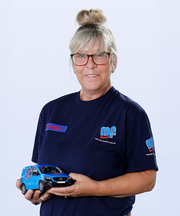 Eine Frau mit blonden Haaren und Brille hält ein Modell eines blauen Mercedes-Vans in der Hand und lächelt freundlich.