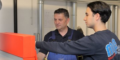 Zwei Fachleute arbeiten an einer technischen Maschine Der erfahrene Techniker zeigt dem Lehrling, wie man eine Maschine bedient, während sie konzentriert schauen.