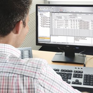 Ein Mann sitzt an einem Schreibtisch und arbeitet konzentriert an einem Computer mit einer Tabellenkalkulation auf dem Bildschirm.
