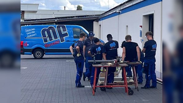 Eine Gruppe von Handwerkern in blauen Arbeitsanzügen versammelt sich um einen Tisch, um an einem Projekt zu arbeiten.