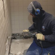 Ein Handwerker arbeitet in einem engen Raum mit einem elektrischen Werkzeug, um Fliesen zu entfernen.