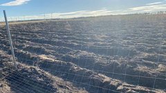 Ein weitläufiges Feld mit frisch gepflügtem Boden, umgeben von einem Zaun und unter einem klaren blauen Himmel.