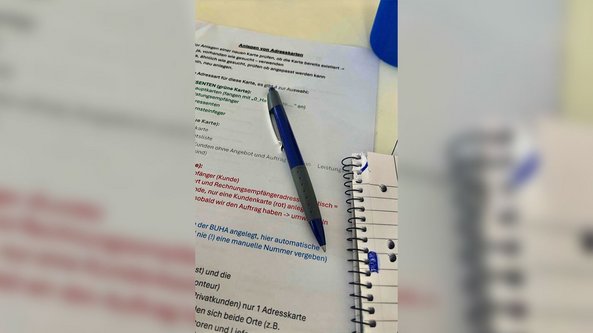 Auf einem Tisch liegen mehrere Dokumente mit bunten Textmarkierungen und einem blauen Kugelschreiber, der darauf zeigt.