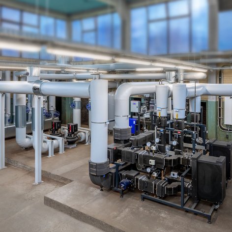 Ein industrieller Raum mit zahlreichen Rohren und Pumpen, die für die Wasserzirkulation in einem technischen System verantwortlich sind.