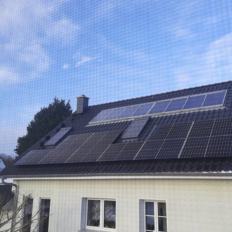 Ein modernes Haus mit einem Dach voller Solarpanels, das unter einem klaren blauen Himmel steht.