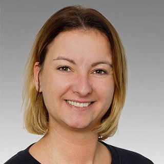 Porträt einer freundlichen Frau mit kurzen Haaren Eine lächelnde Frau mit schulterlangen, blonden Haaren und einem freundlichen Ausdruck vor einem grauen Hintergrund.