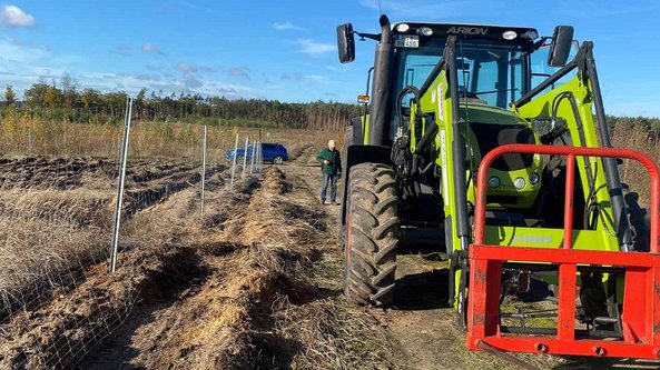 Ein grüner Traktor steht auf einem Feld, während ein Mann in einem grünen Mantel in der Nähe steht und den Boden betrachtet.