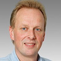 Professionelles Porträt eines lächelnden Mannes Ein Mann mit blonden Haaren und blauen Augen lächelt freundlich in die Kamera, vor einem grauen Hintergrund.