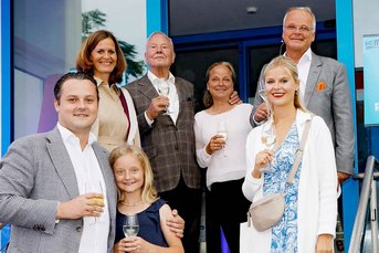 Eine fröhliche Gruppe von sieben Personen posiert vor einem Kino mit Gläsern in der Hand, um einen besonderen Anlass zu feiern.